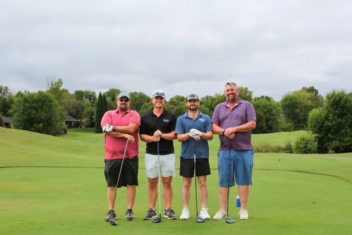 Four golfers in pink, black, blue, and purple shirts posing on the green.