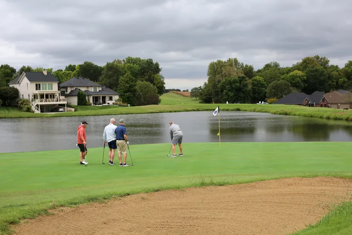 Participants putting on a lakeside green near a sand bunker.