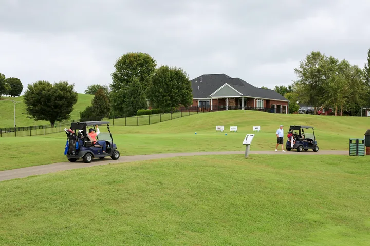 Golf carts on the course near a building and sponsor signs.